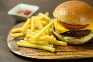Classic burger with cheese and fries served on a wooden cutting board.